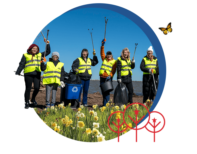 Cut-out graphic with no badge: six women in yellow hi-vis vests cheer with litter grabbers raised beside a blue recycling box, a black bucket and rubbish sacks on a lakeside beach, set inside a circle with daffodils in the foreground, red line-drawn trees at the bottom and a monarch butterfly at the upper right.