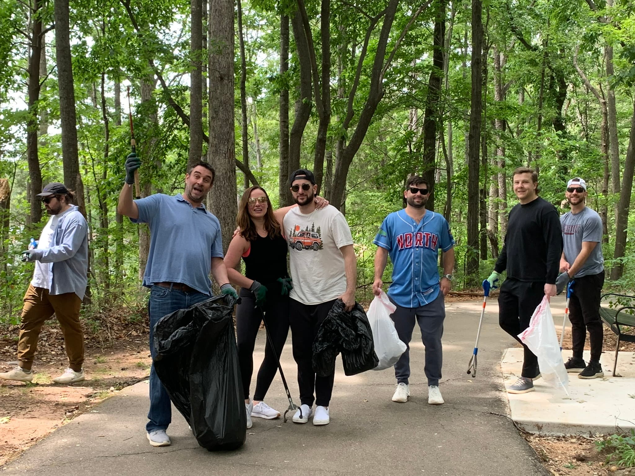 Small view of six people with black trash bags and grabbers standing on a paved trail in a leafy forest