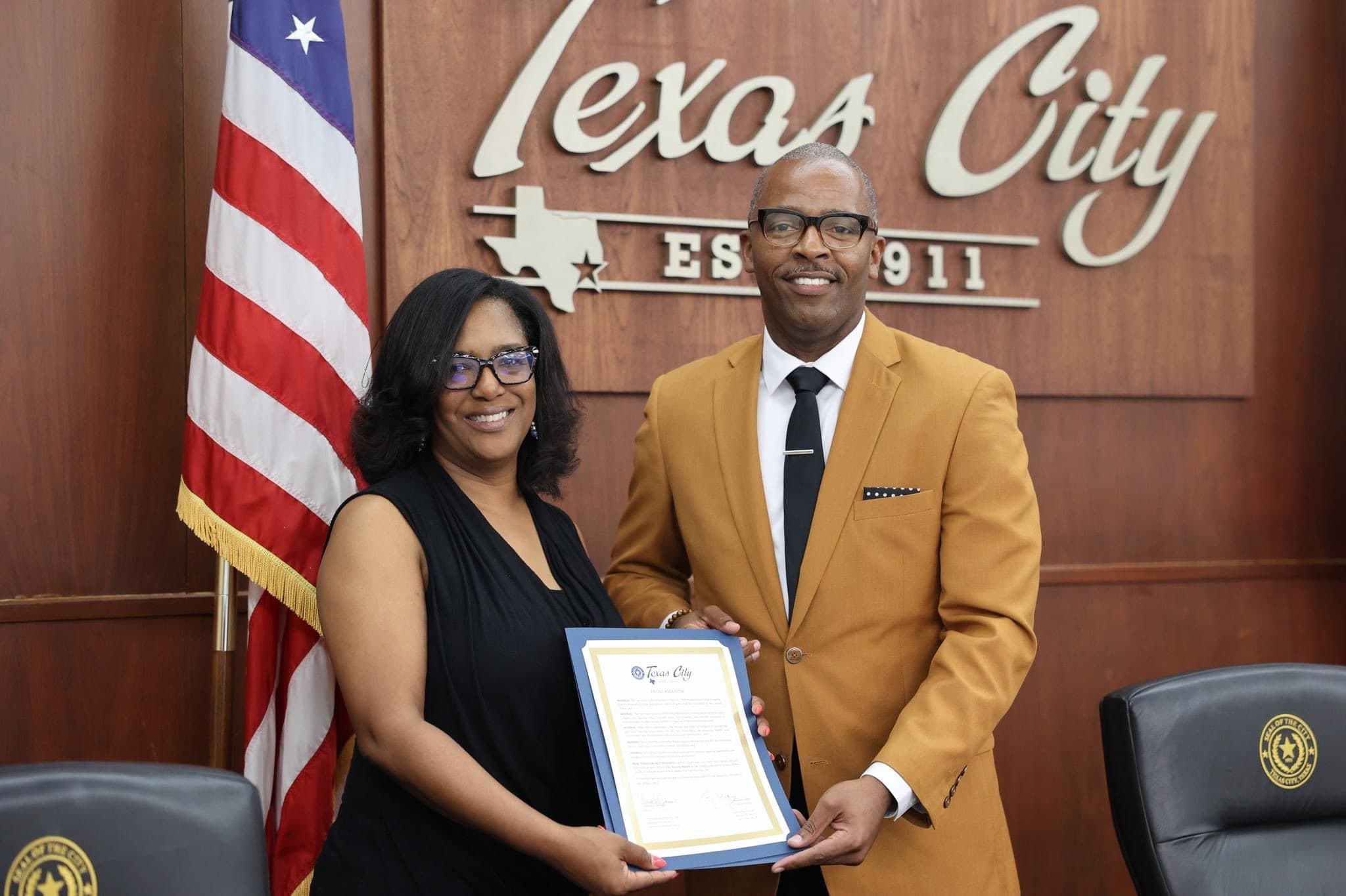 Small view of a proclamation presentation between two people beside an American flag under a city wall seal