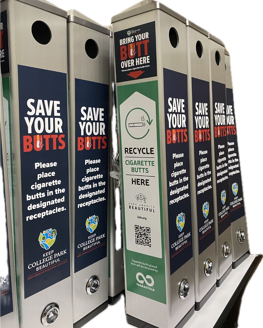 Half a dozen new steel cigarette receptacles lined up side by side, most wrapped in navy panels reading SAVE YOUR BUTTS with a Keep College Park Beautiful logo; the centre one is green and reads RECYCLE CIGARETTE BUTTS HERE with a QR code and a BRING YOUR BUTT OVER HERE topper.