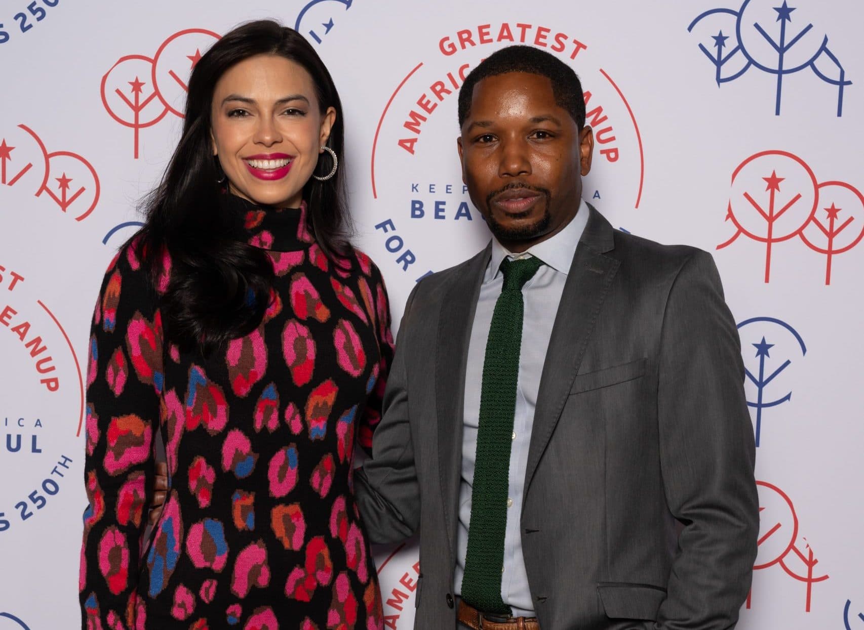 Woman in a pink and black animal-print dress with a man in a grey suit and knitted green tie at the branded wall