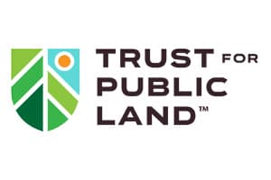 Logo on white: a shield shape filled with green wedges, a blue sky panel and an orange sun, beside the dark stacked words TRUST FOR PUBLIC LAND.
