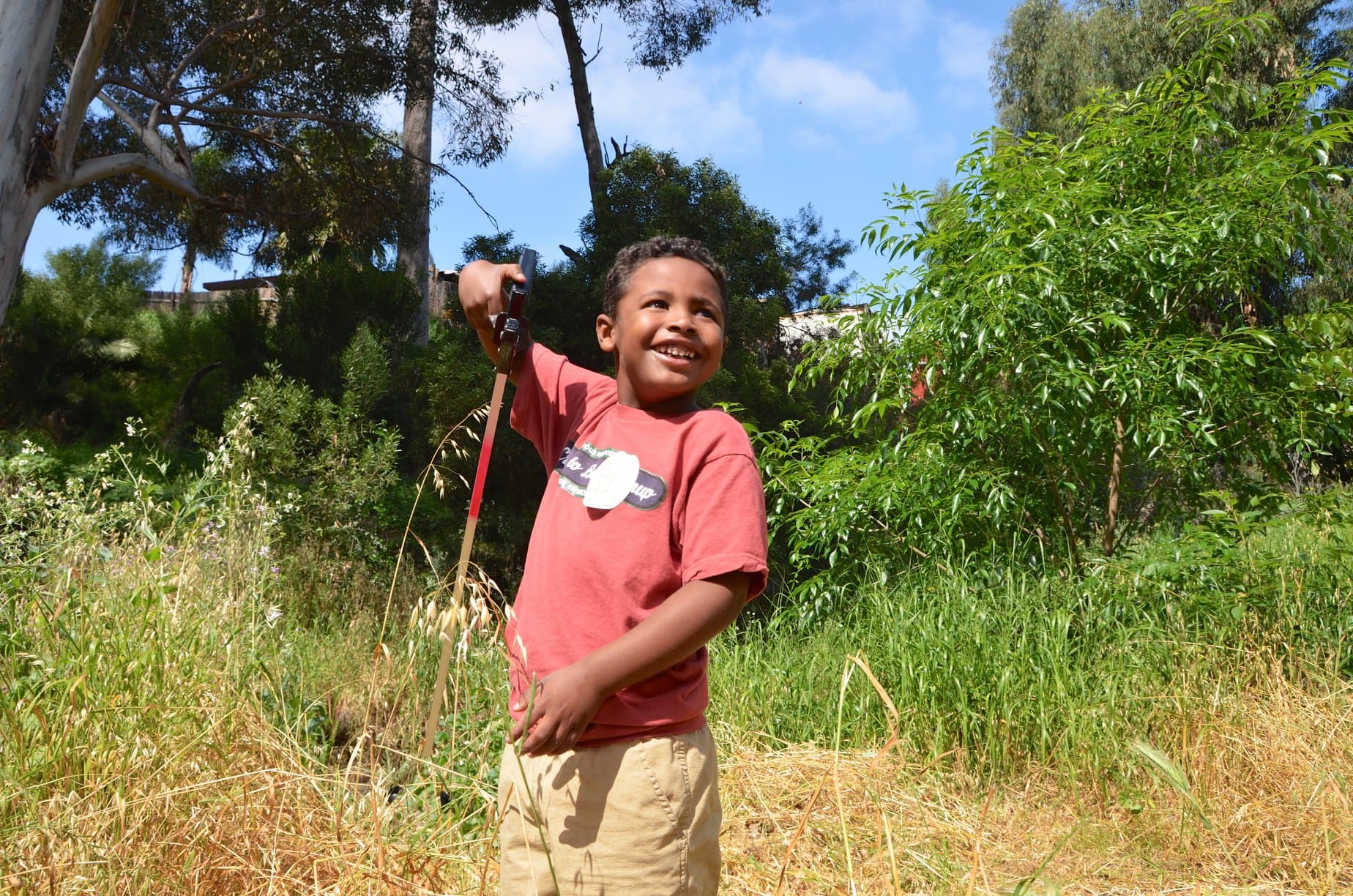 A young volunteer crouching at a creek bank during a Creek to Bay cleanup, reaching into the grass to pick up a piece of litter.